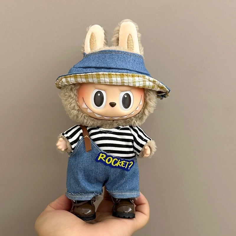 Toy figure with a denim outfit and hat held in a hand against a plain background